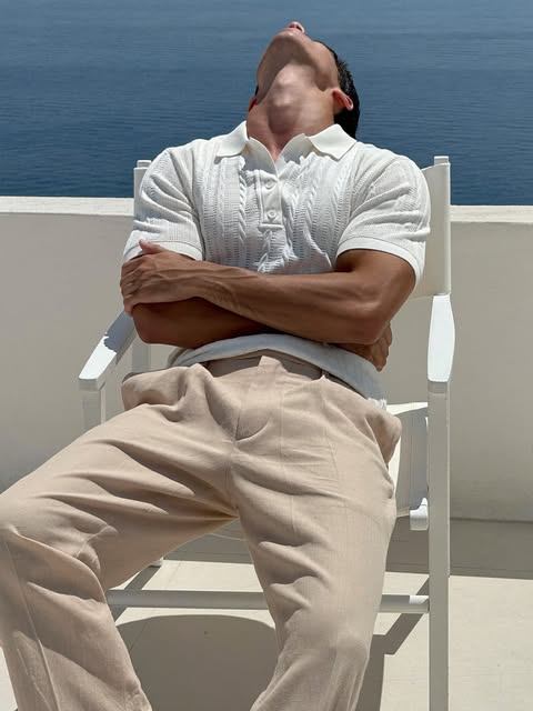 Man in white knit polo seated on a stone chair with face lifted to the sun