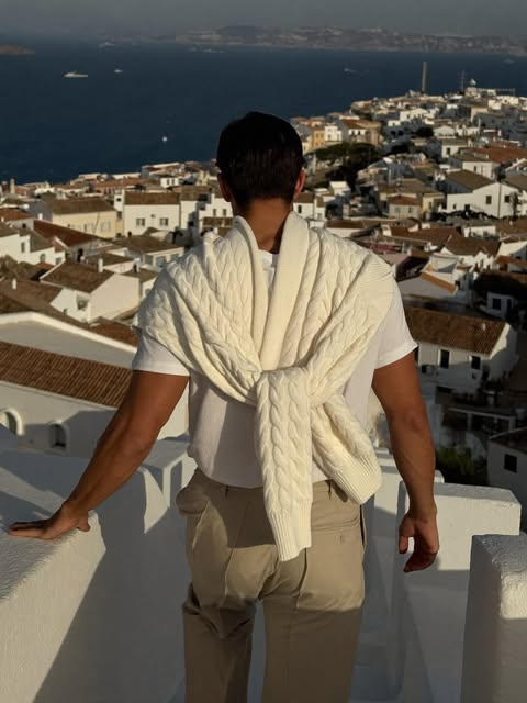 Man from behind descending a whitewashed coastal staircase with ivory cable knit over shoulders