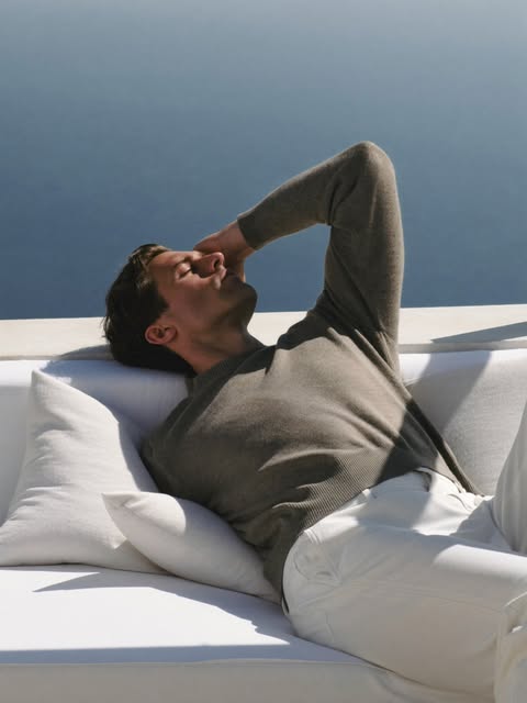 Man in a taupe sweater resting on a daybed by the sea