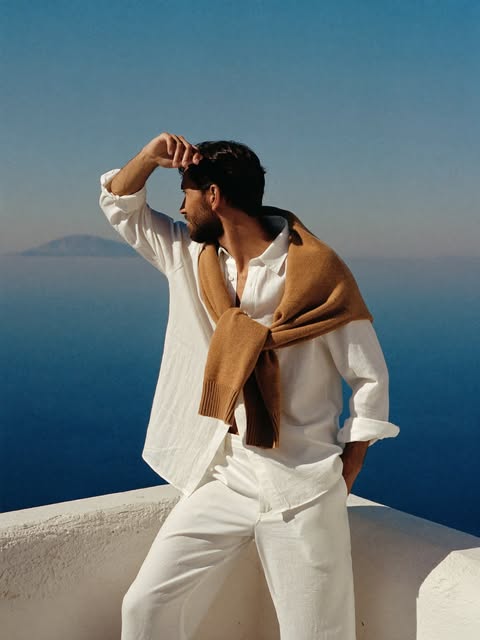Man with a camel knit draped over his shoulders looking towards the coast