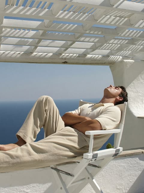 Man in an ivory knit polo reclining beneath a coastal pergola